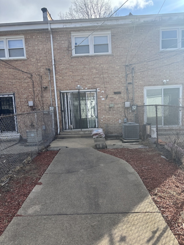 back of property featuring brick siding, cooling unit, and fence