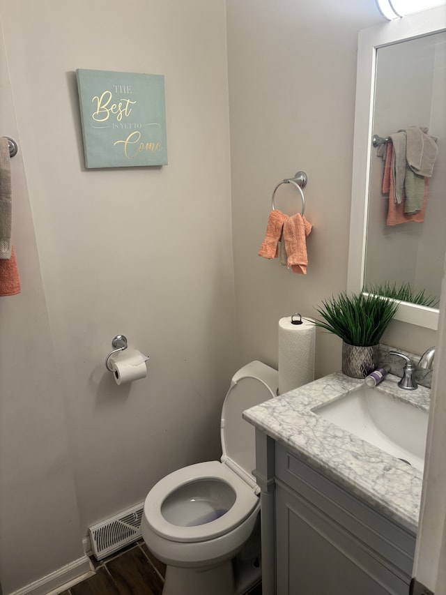 half bathroom featuring visible vents, toilet, vanity, wood finished floors, and baseboards