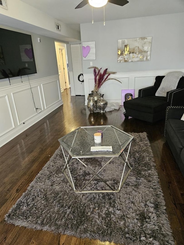 living area with visible vents, a ceiling fan, wainscoting, wood finished floors, and a decorative wall