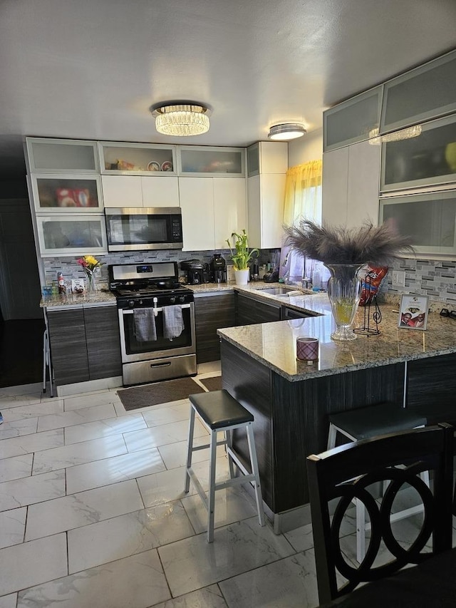 kitchen featuring a breakfast bar, marble finish floor, stainless steel appliances, stone countertops, and a peninsula