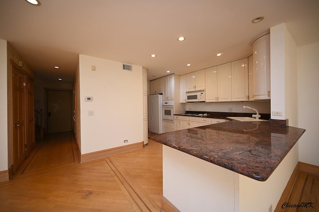 kitchen with white appliances, light wood-style flooring, a peninsula, a sink, and recessed lighting