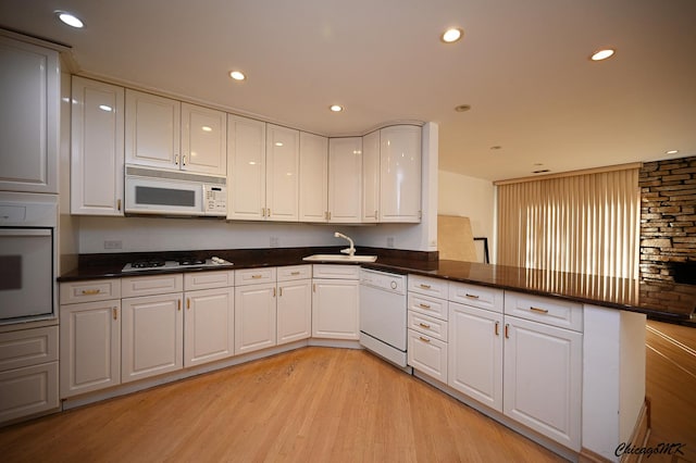 kitchen with light wood-style flooring, white cabinetry, a sink, white appliances, and a peninsula