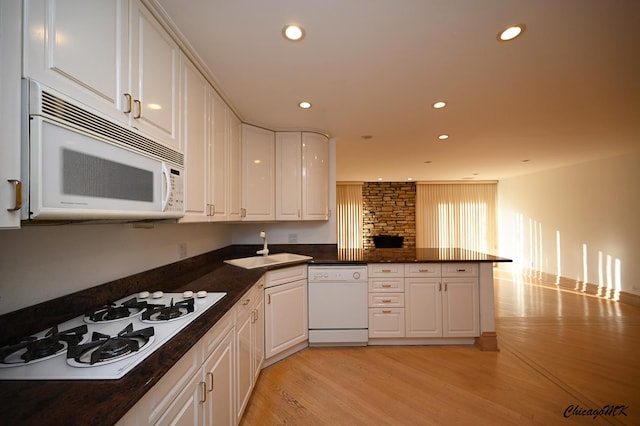 kitchen featuring a peninsula, white appliances, white cabinetry, and a sink