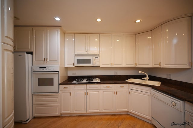 kitchen with white appliances, dark countertops, a sink, and recessed lighting