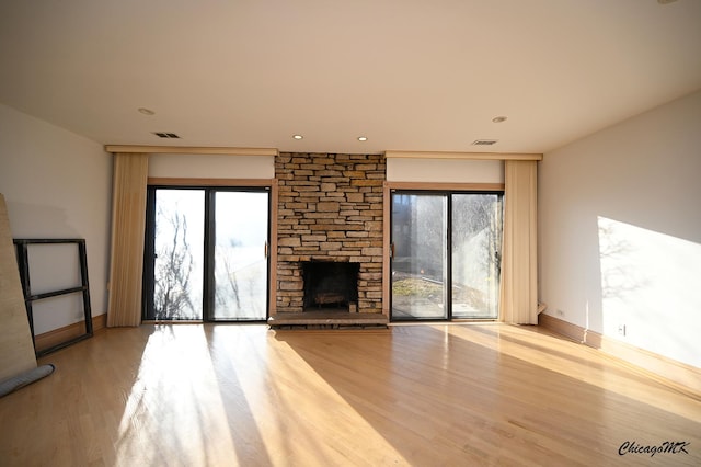 unfurnished living room featuring a stone fireplace, visible vents, a wealth of natural light, and wood finished floors