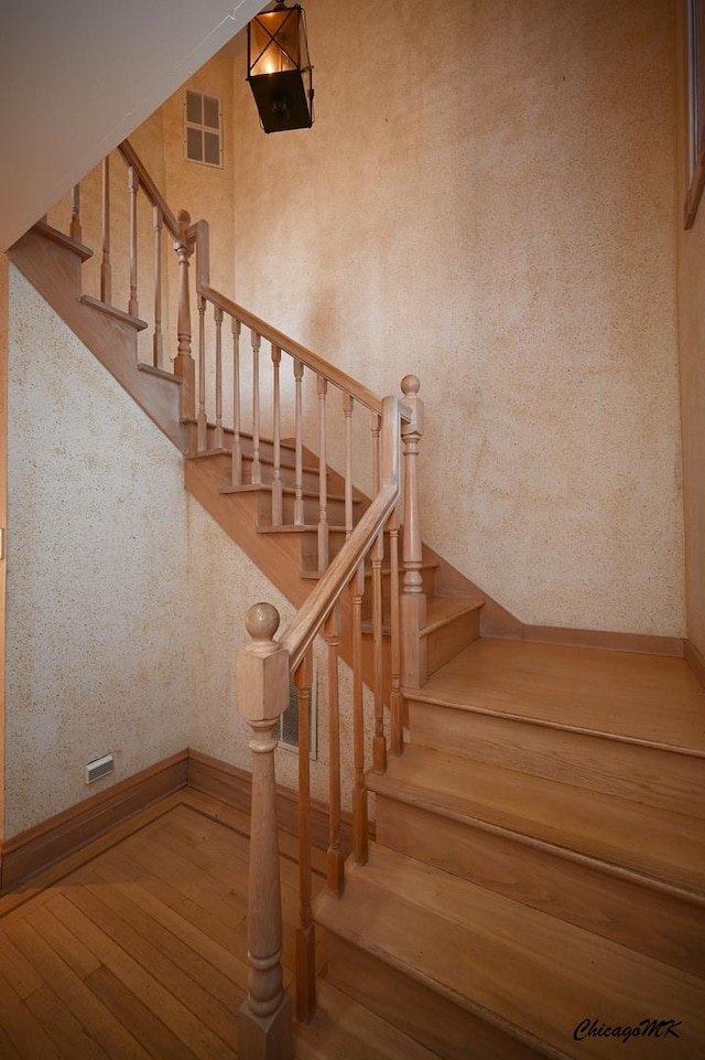 stairway with baseboards, hardwood / wood-style floors, visible vents, and wallpapered walls