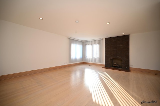 unfurnished living room with a brick fireplace, baseboards, and light wood-style floors