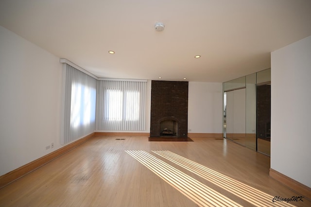 unfurnished living room with light wood-style floors, a brick fireplace, and baseboards