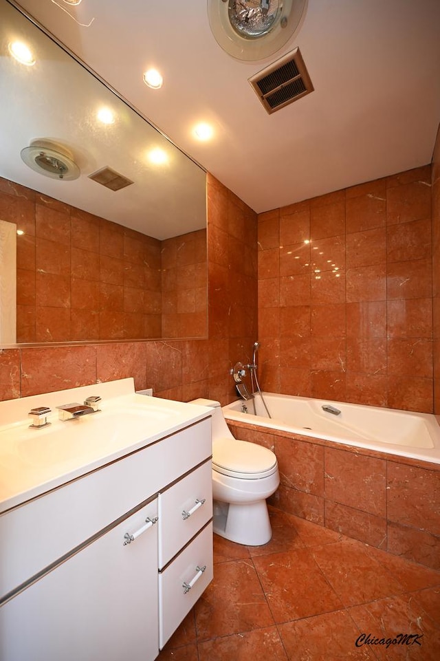 full bathroom with toilet, a relaxing tiled tub, visible vents, vanity, and tile walls