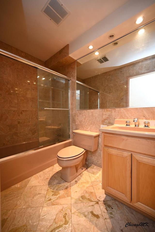 bathroom featuring visible vents, shower / bath combination with glass door, tile walls, and toilet