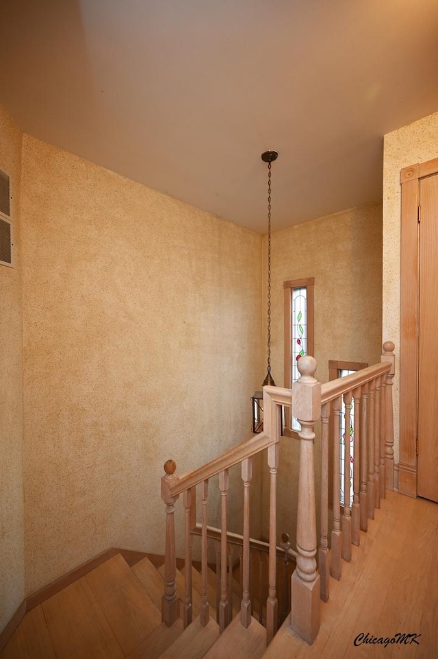 stairs featuring wood finished floors and wallpapered walls