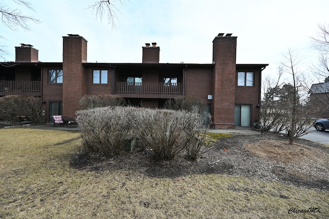 back of property with a balcony, a chimney, a lawn, and brick siding