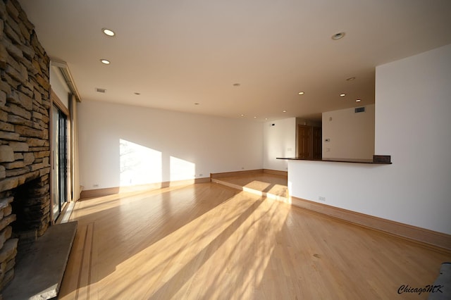 unfurnished living room with light wood-type flooring, recessed lighting, visible vents, and a stone fireplace