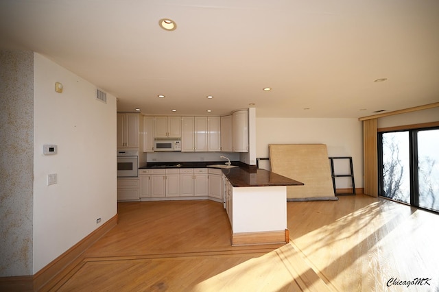 kitchen featuring white appliances, visible vents, white cabinets, dark countertops, and a peninsula