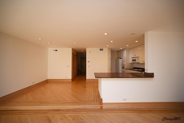 kitchen featuring white appliances, light wood finished floors, dark countertops, white cabinetry, and recessed lighting