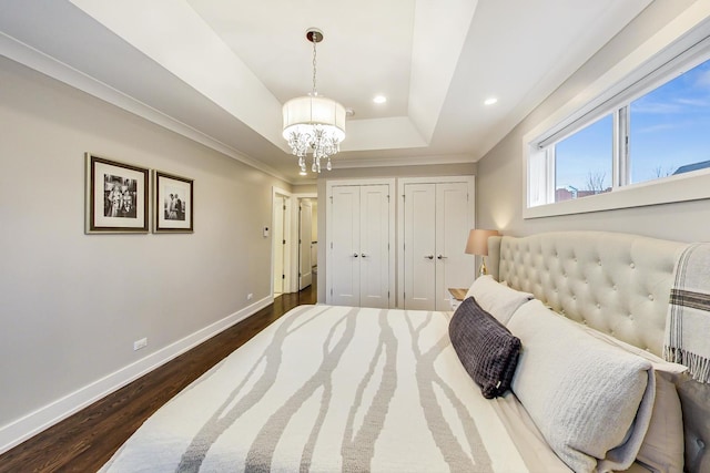 bedroom with a tray ceiling, multiple closets, dark wood-type flooring, a chandelier, and baseboards