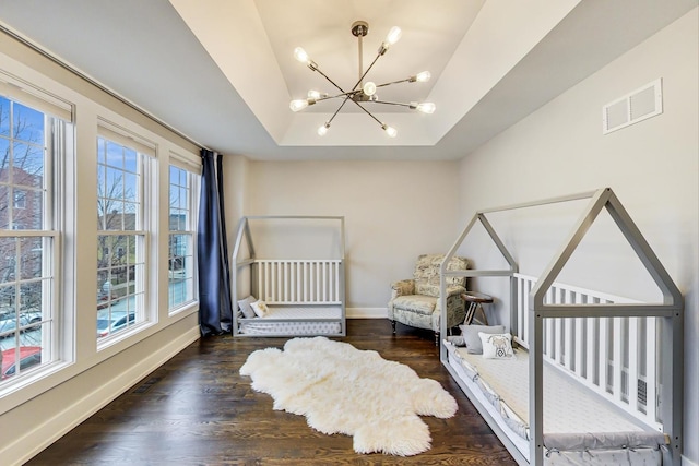 bedroom with a notable chandelier, wood finished floors, visible vents, baseboards, and a tray ceiling