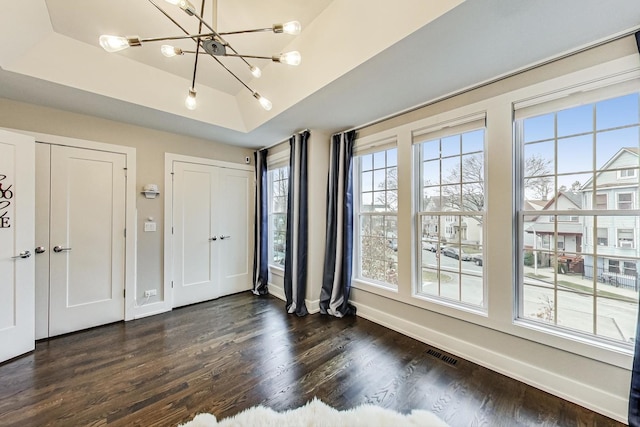 unfurnished bedroom with baseboards, visible vents, a raised ceiling, and dark wood-type flooring