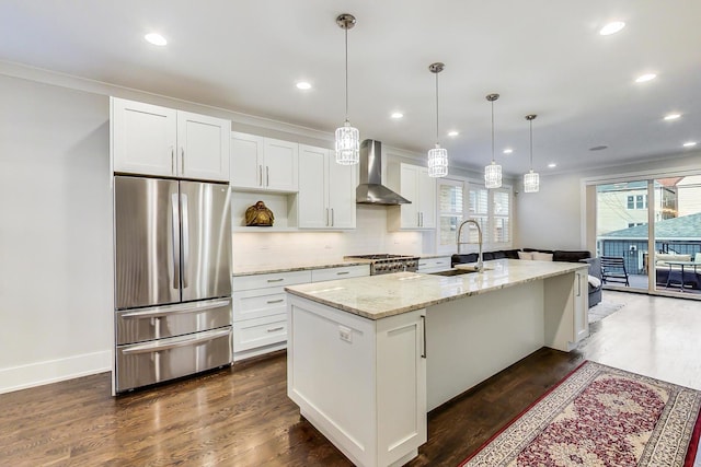 kitchen featuring white cabinets, freestanding refrigerator, a kitchen island with sink, wall chimney range hood, and a sink