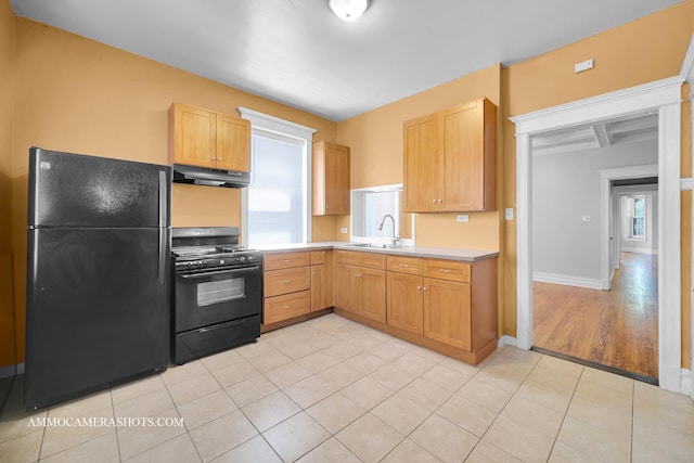 kitchen featuring light countertops, a sink, plenty of natural light, under cabinet range hood, and black appliances