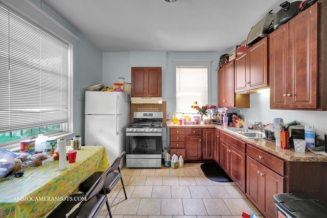 kitchen with light tile patterned floors, freestanding refrigerator, a sink, under cabinet range hood, and stainless steel gas range oven