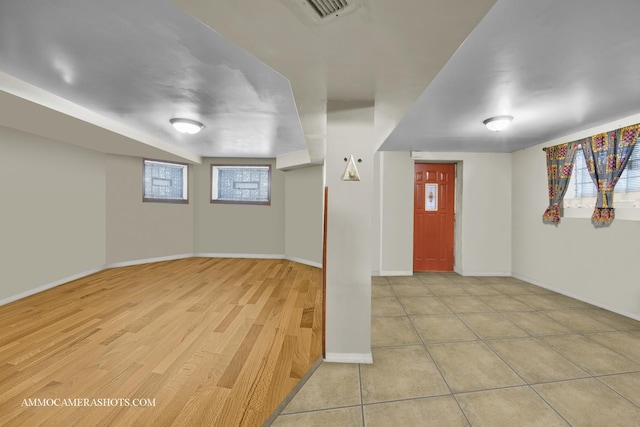 basement featuring light wood-style flooring, visible vents, baseboards, and a wealth of natural light