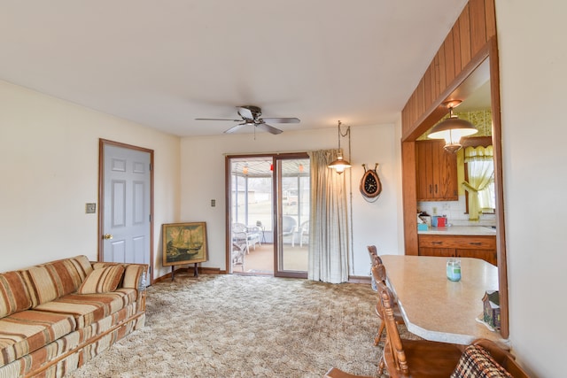 living area featuring ceiling fan, baseboards, and carpet flooring