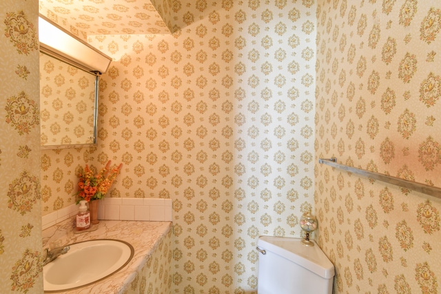 bathroom featuring toilet, wallpapered walls, and a sink