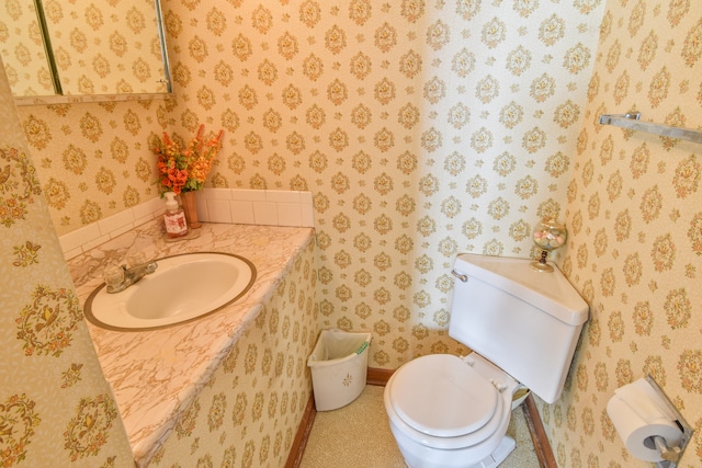 bathroom with toilet, wallpapered walls, and vanity