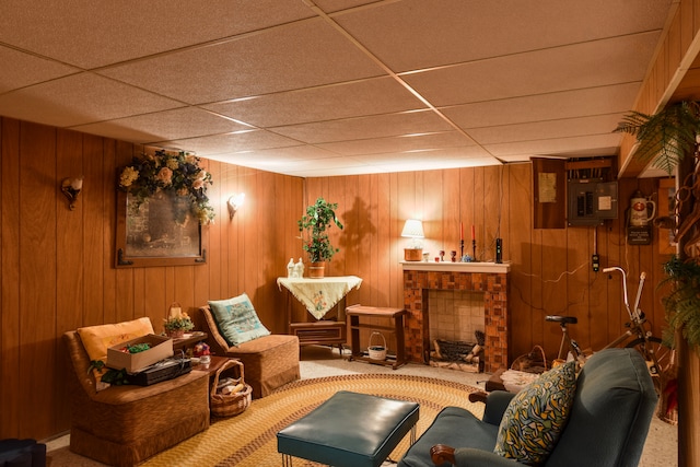 sitting room with wooden walls, a fireplace, a drop ceiling, and carpet flooring