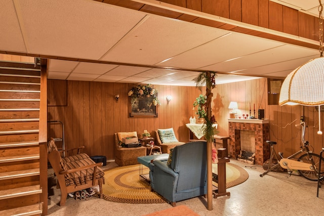 living area with stairs, wood walls, a fireplace, and a paneled ceiling