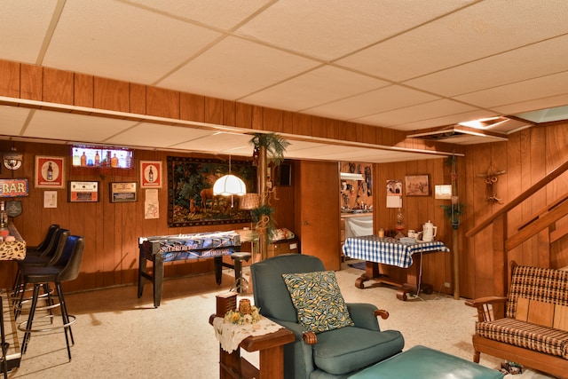 living area with stairs, a paneled ceiling, and wooden walls