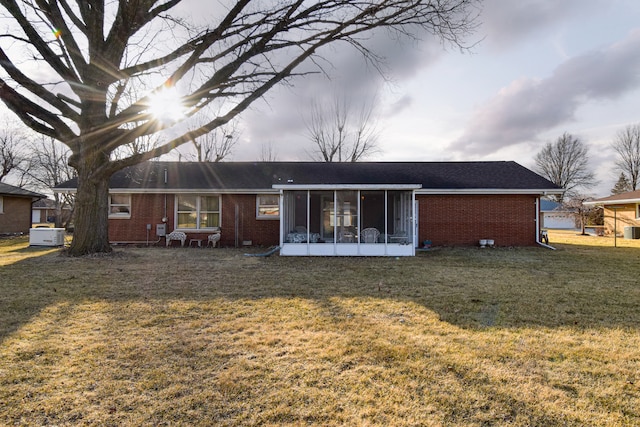 rear view of house featuring a yard, a sunroom, and brick siding