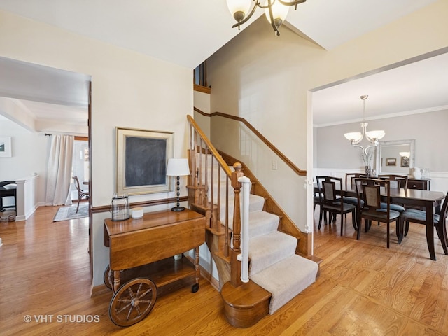 stairs with an inviting chandelier, wood finished floors, and crown molding