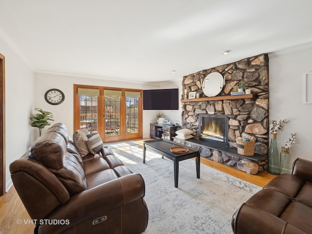 living area with a stone fireplace, crown molding, wood finished floors, and baseboards