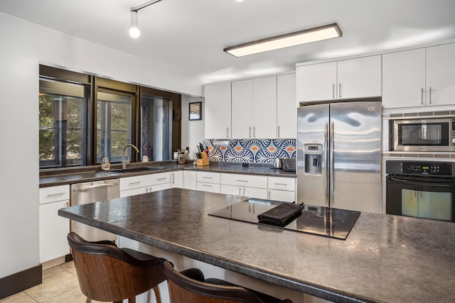 kitchen with black appliances, a sink, tasteful backsplash, dark countertops, and a breakfast bar area