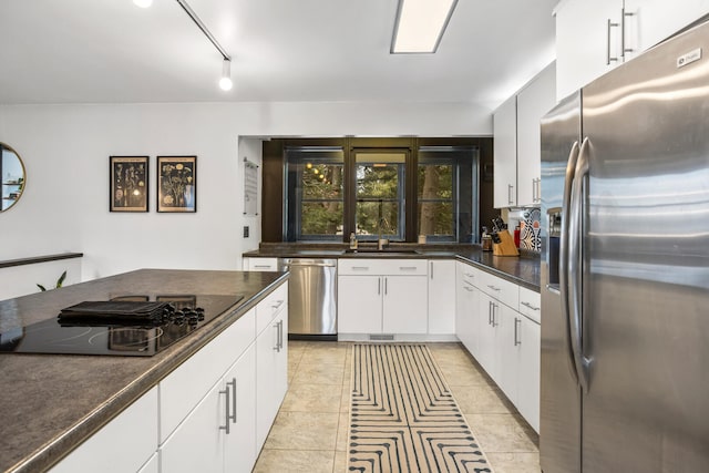 kitchen with light tile patterned floors, a sink, white cabinets, appliances with stainless steel finishes, and dark countertops