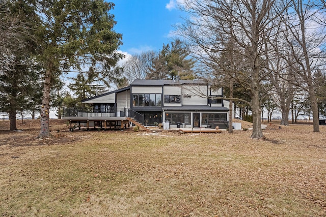 back of property with a deck, a lawn, and a sunroom