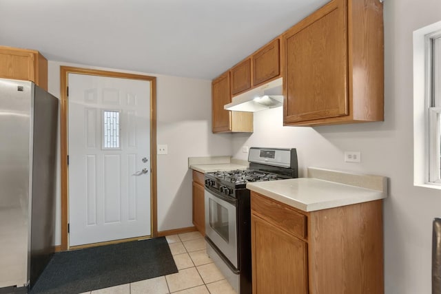 kitchen with light tile patterned floors, appliances with stainless steel finishes, brown cabinets, light countertops, and under cabinet range hood