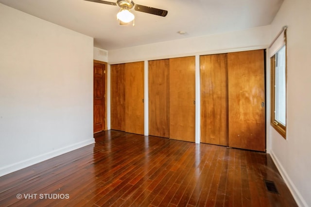 unfurnished bedroom with wood-type flooring, visible vents, baseboards, and multiple closets