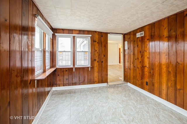 empty room with visible vents, wooden walls, and baseboards