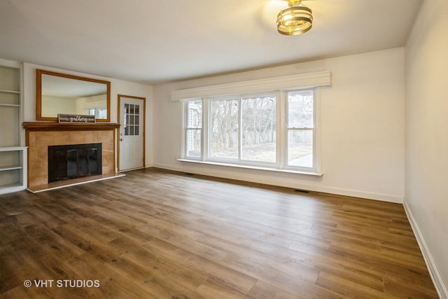 unfurnished living room featuring dark wood-style floors, a tile fireplace, visible vents, and baseboards