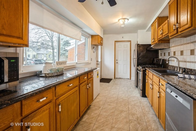 kitchen with tasteful backsplash, brown cabinetry, dark stone countertops, stainless steel appliances, and a sink