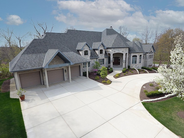 french provincial home with stone siding, driveway, a chimney, and an attached garage