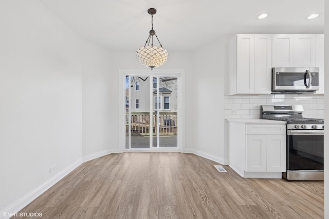 kitchen featuring appliances with stainless steel finishes, light wood-style flooring, baseboards, white cabinets, and backsplash
