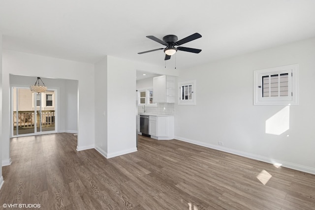 unfurnished living room featuring wood finished floors, baseboards, ceiling fan, and a sink