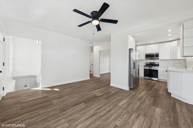 kitchen featuring appliances with stainless steel finishes, open floor plan, dark wood-type flooring, a sink, and white cabinetry