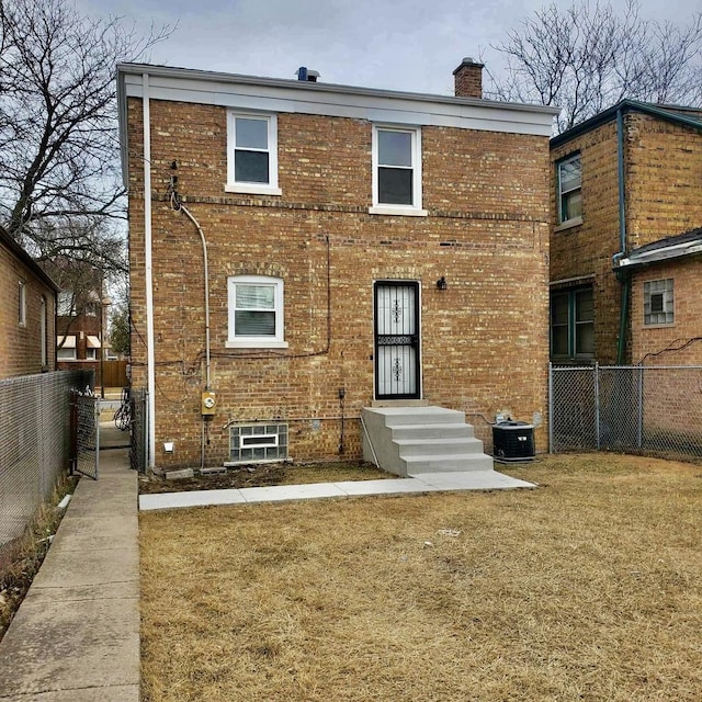 back of property with entry steps, central AC unit, a chimney, fence, and brick siding