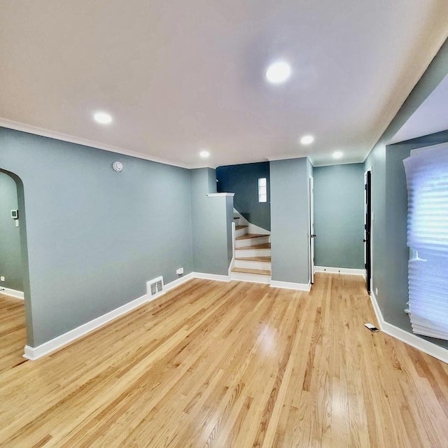 below grade area with arched walkways, wood finished floors, visible vents, baseboards, and stairway