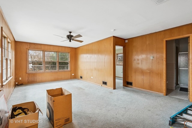 carpeted living room featuring a ceiling fan, visible vents, wood walls, and baseboards